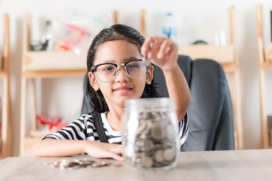 little girl in putting coin in to glass jar for saving money