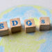 Wooden blocks spelling out the letters S. D. G. s. sit above a drawing of the Earth.