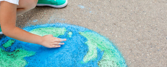 Un enfant dessine la planète Terre avec de la craie.