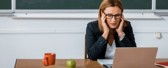 Une enseignante ressent des maux de tête en étant assise à son bureau, devant son ordinateur.