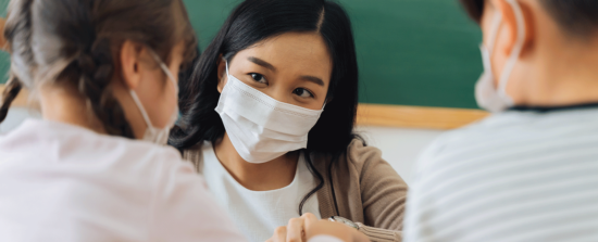 Teacher helping two student wearing masks